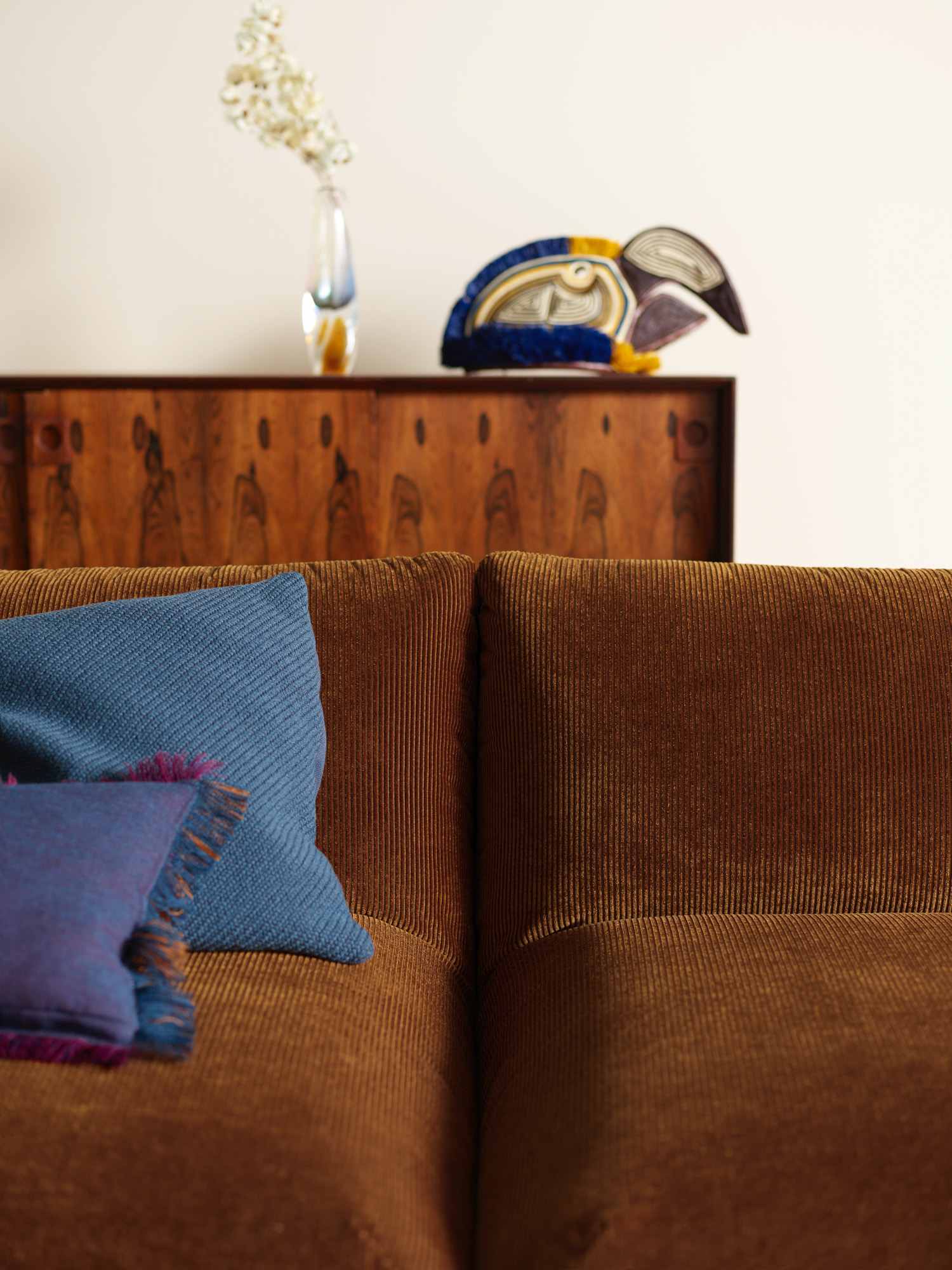 Gros plan du dossier Jalis en velours côtelé brun, accompagné d’un coussin bleu.
