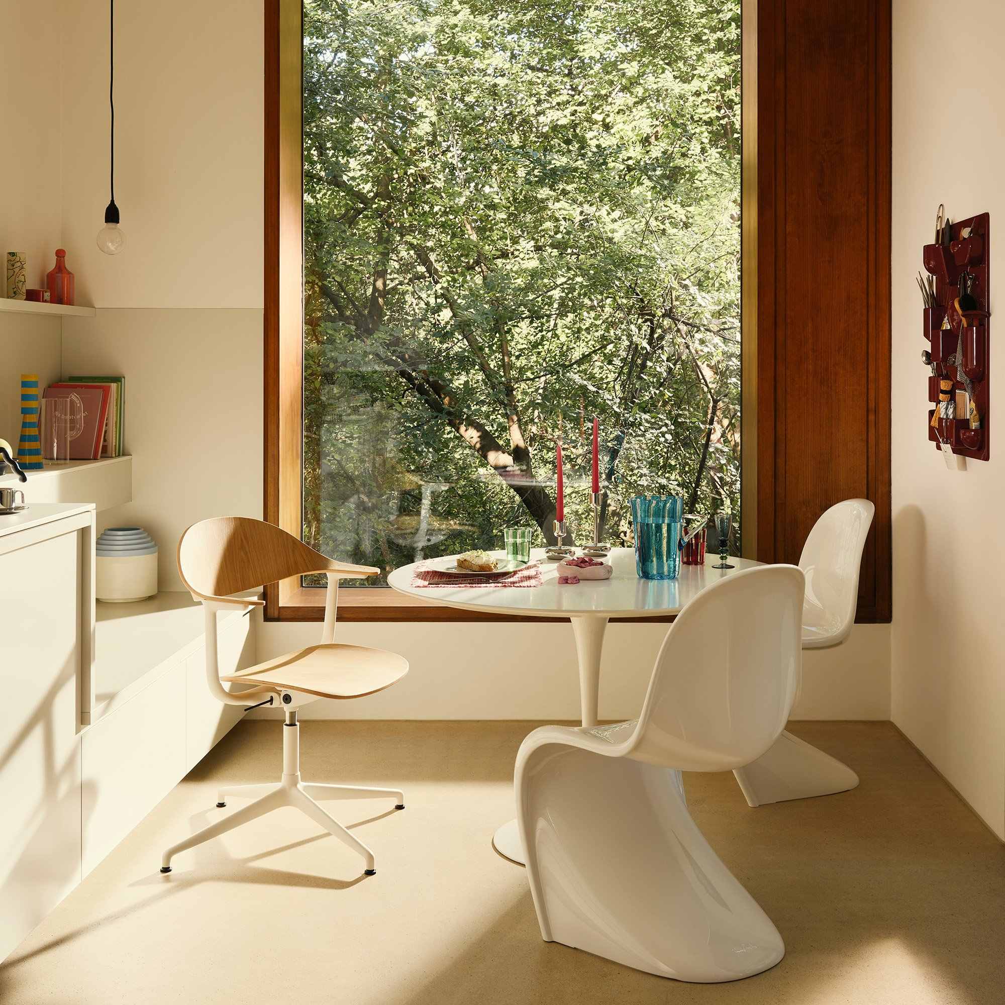 Chaises Panton blanches autour d’une table ronde près d’une fenêtre ouverte sur les arbres