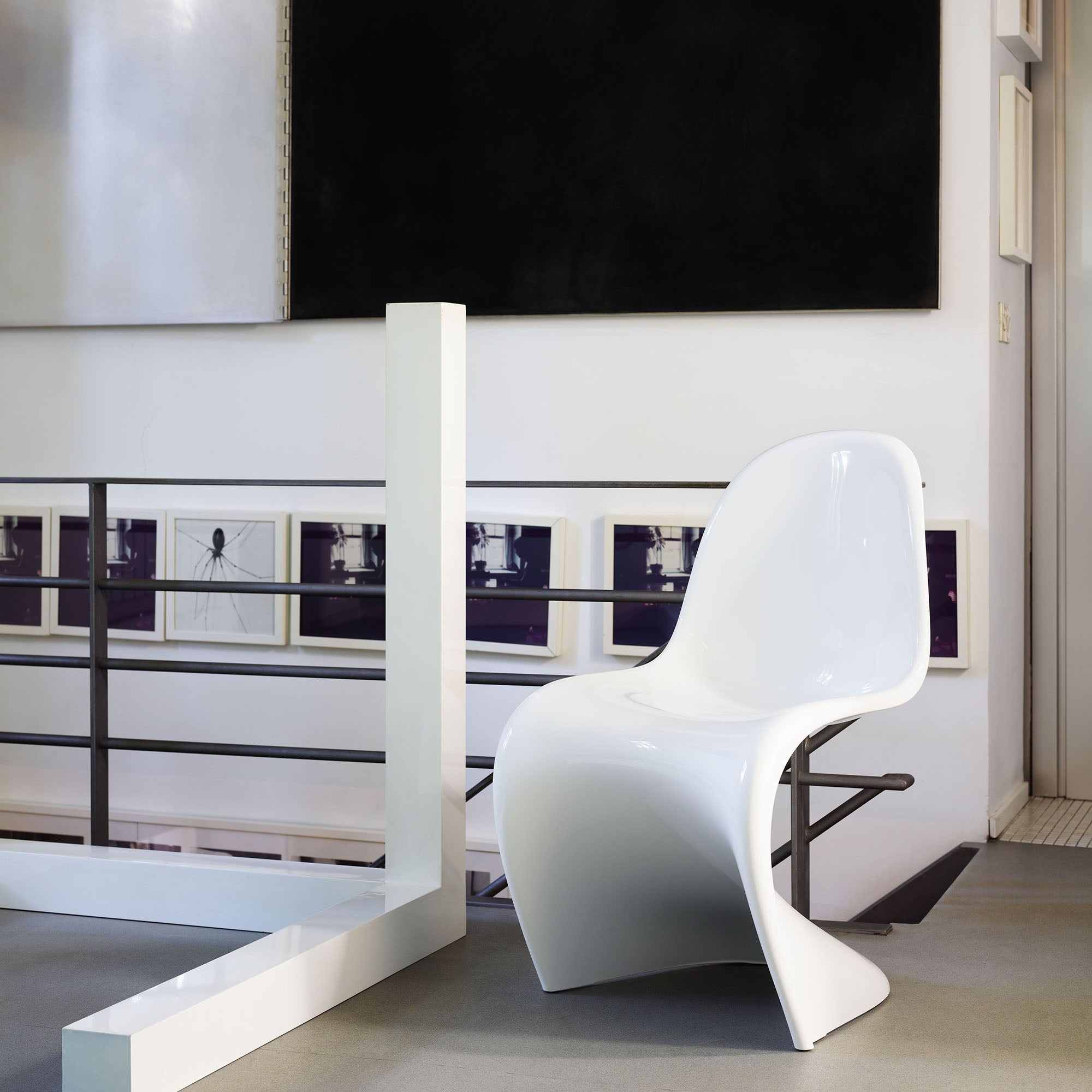 Chaise Panton blanche dans une galerie avec escalier et œuvres en noir et blanc