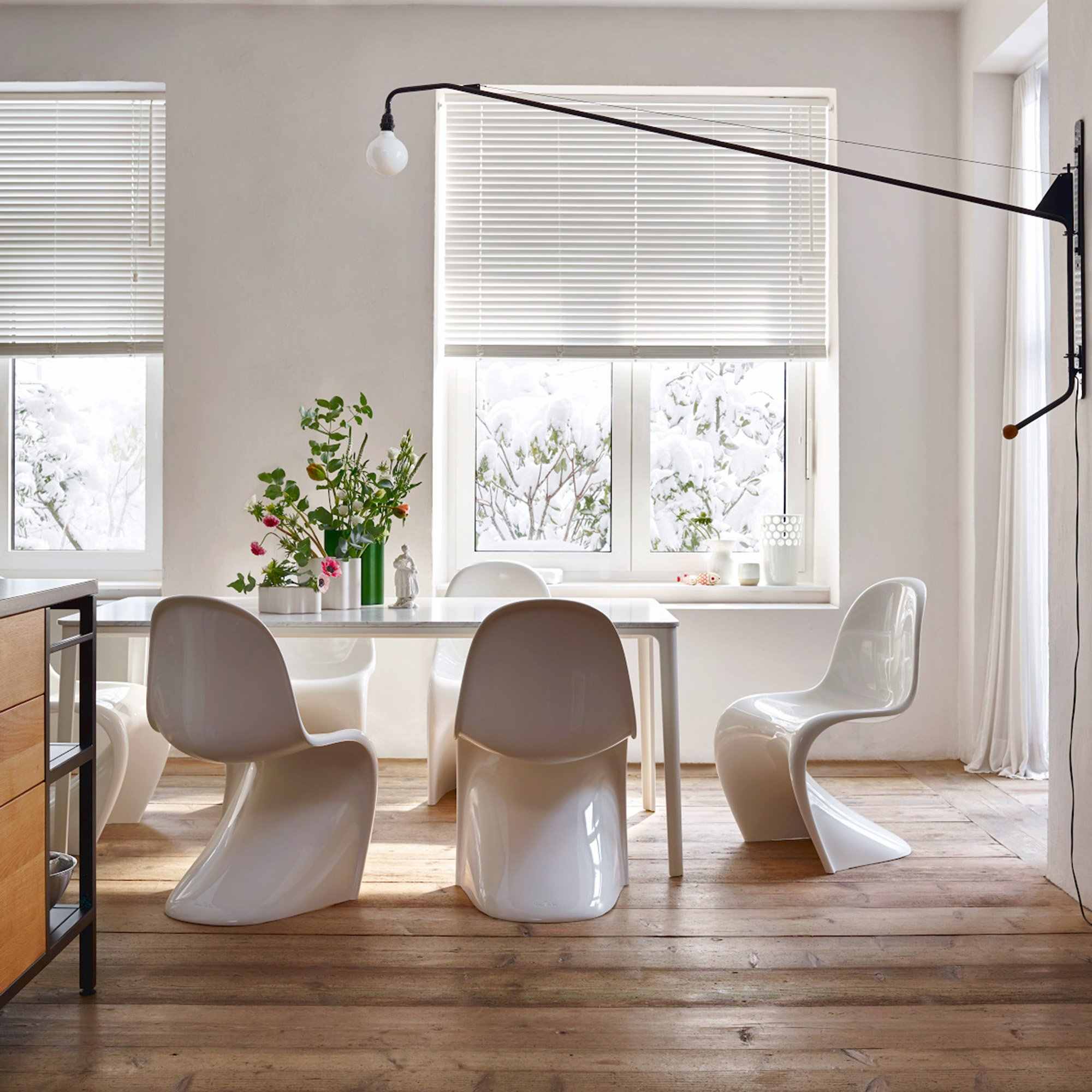 Chaises Panton blanches dans une salle à manger épurée, sol en bois et stores blancs