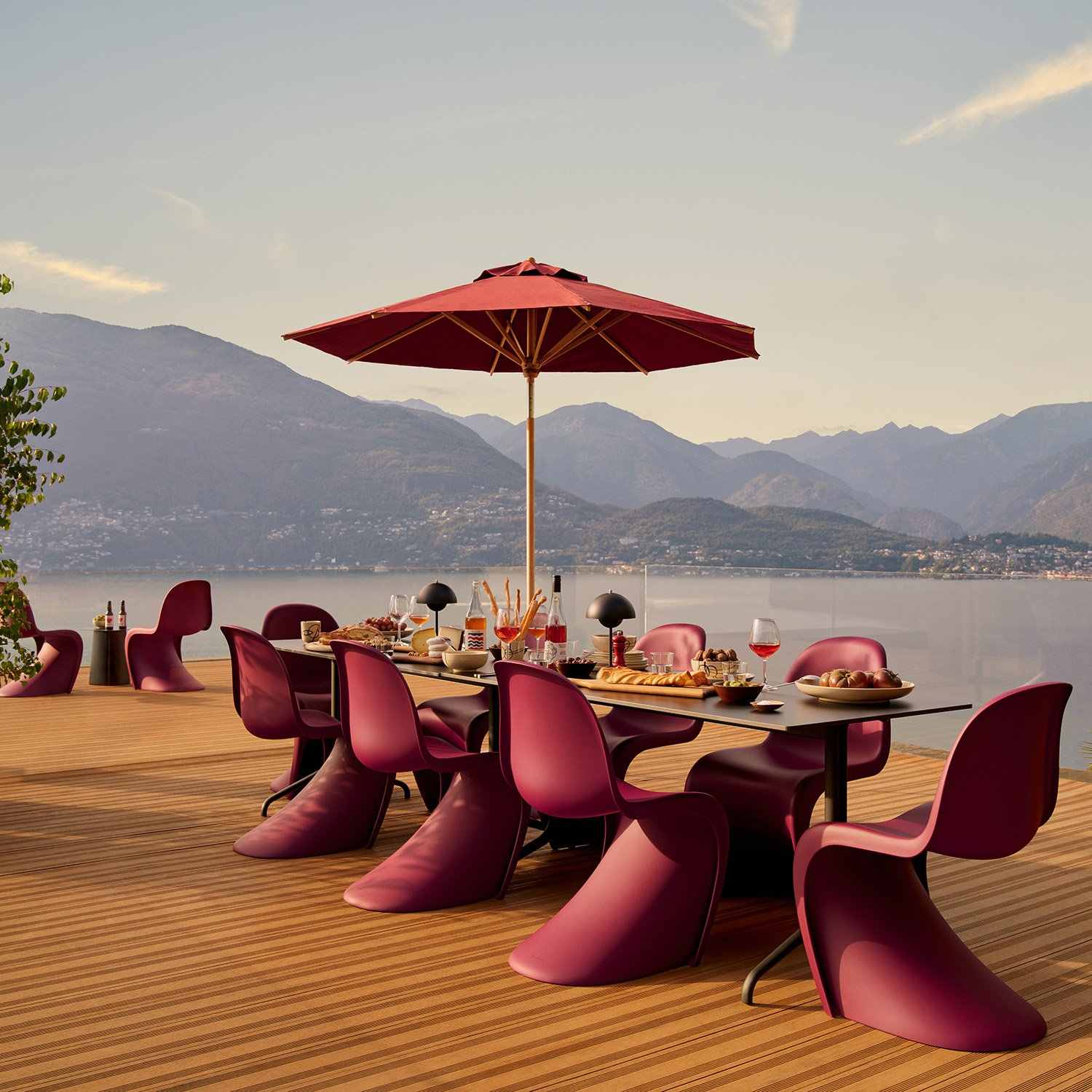 Chaises Panton bordeaux autour d’une grande table sur une terrasse face à un lac et aux montagnes