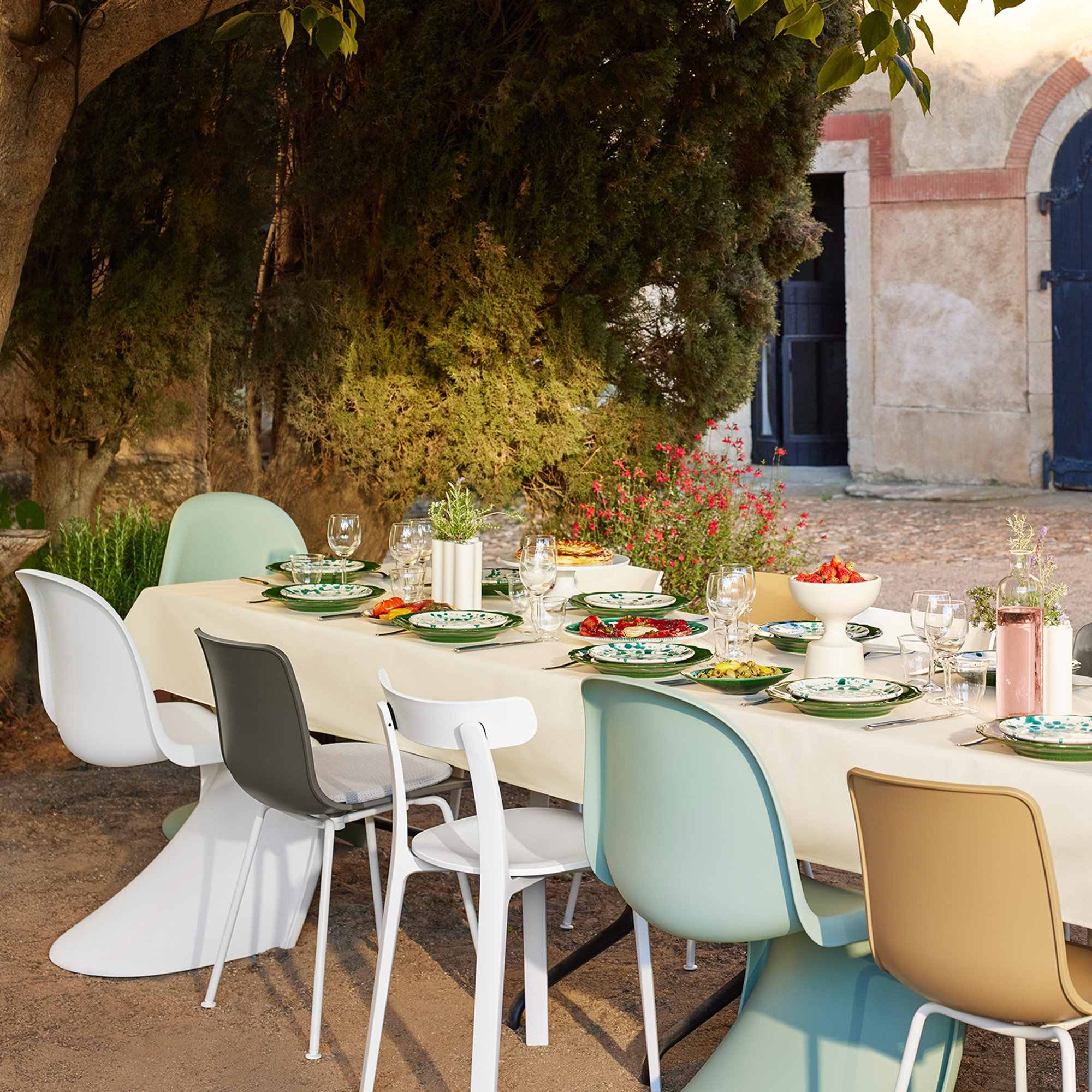 Chaises Panton vert menthe et blanches parmi les assises d’une table dans une cour arborée