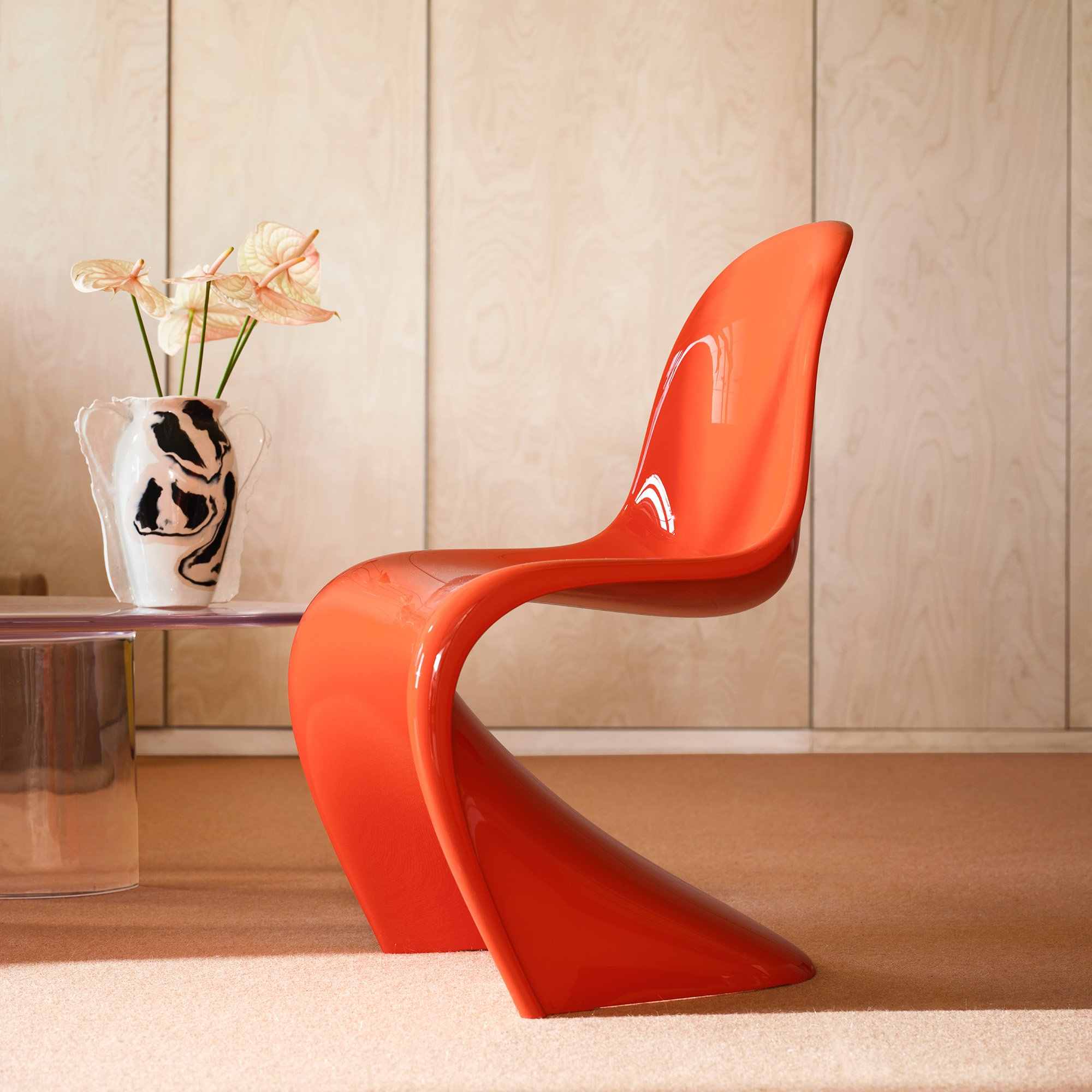 Chaise Panton rouge orangé devant des panneaux de bois clair, photographie de référence Vitra