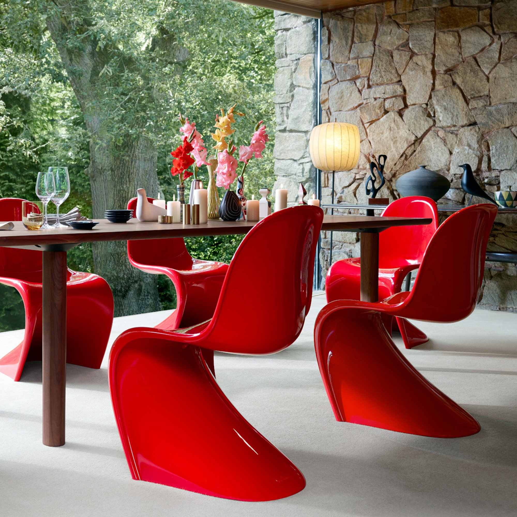 Chaises Panton rouges autour d’une table en bois, devant un mur en pierre et une baie vitrée sur le jardin