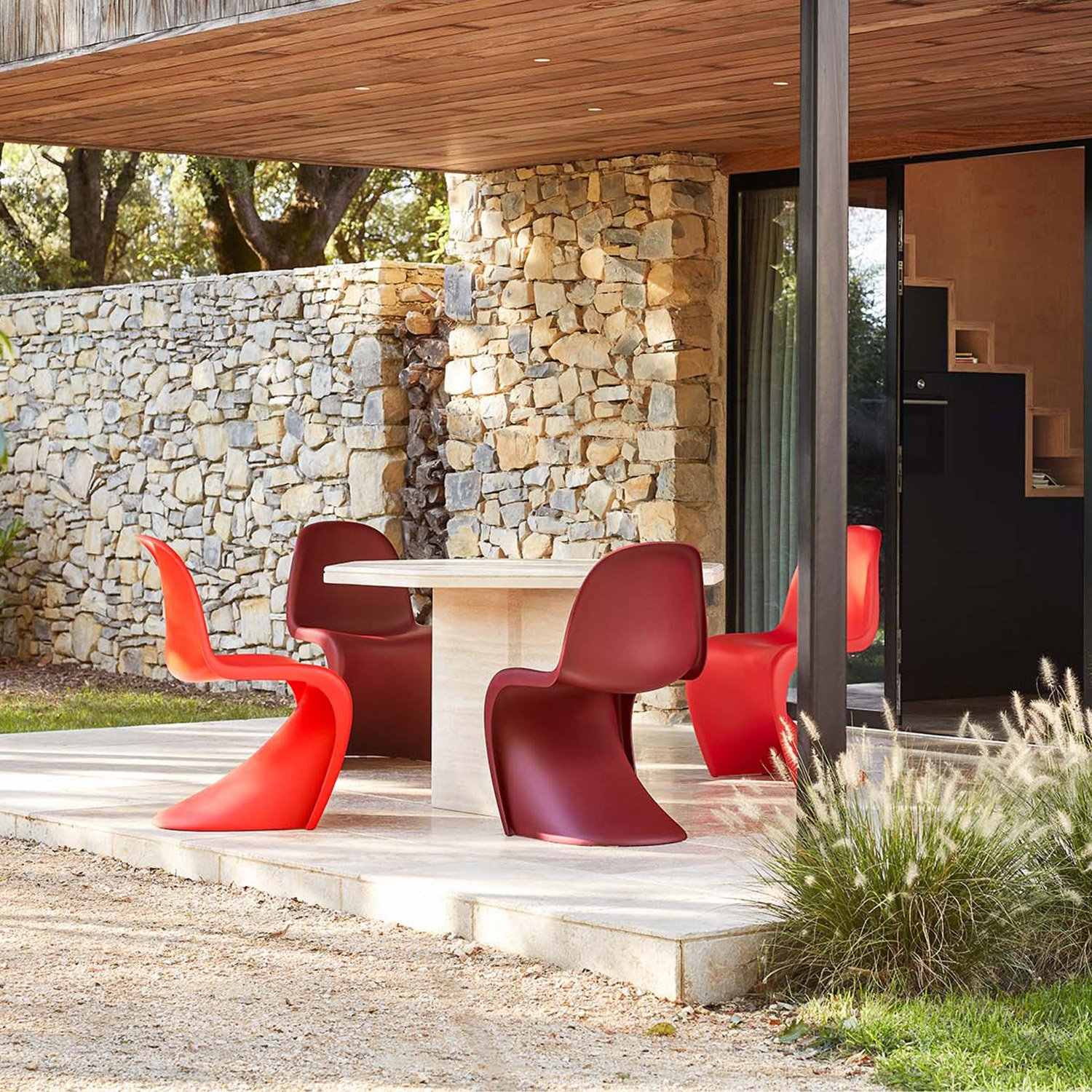 Chaises Panton rouges et bordeaux sur une terrasse couverte avec une table et des murs en pierre